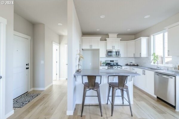 kitchen with light hardwood / wood-style floors, appliances with stainless steel finishes, white cabinets, a breakfast bar, and sink