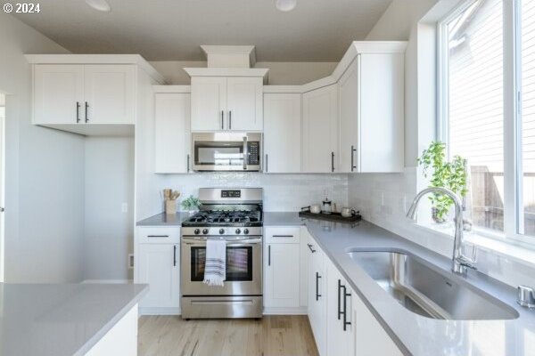 kitchen with white cabinets, appliances with stainless steel finishes, sink, and light hardwood / wood-style flooring