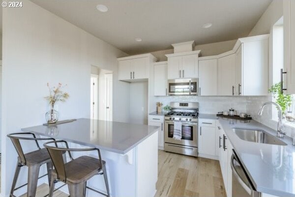 kitchen with white cabinets, stainless steel appliances, sink, backsplash, and a breakfast bar area