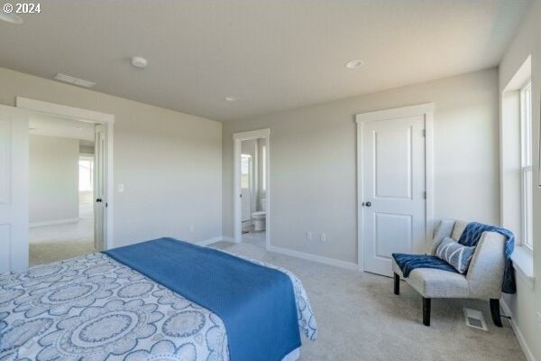 bedroom with light colored carpet, multiple windows, and ensuite bath