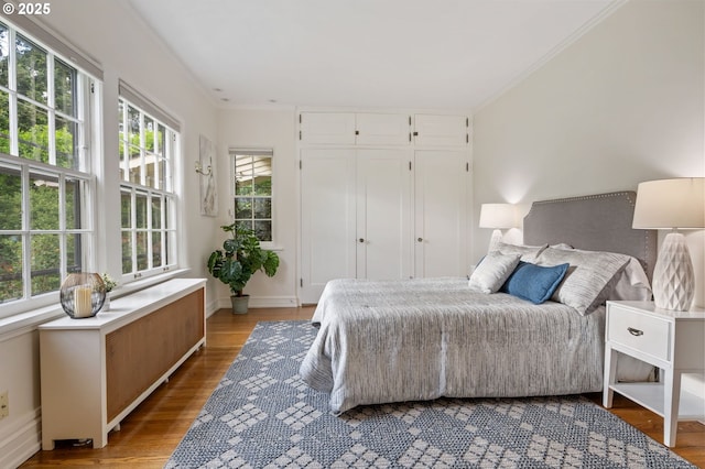 bedroom with multiple windows, light wood finished floors, ornamental molding, baseboards, and a closet