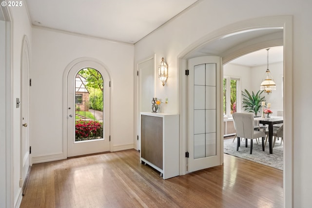 foyer with wood finished floors, arched walkways, baseboards, and crown molding