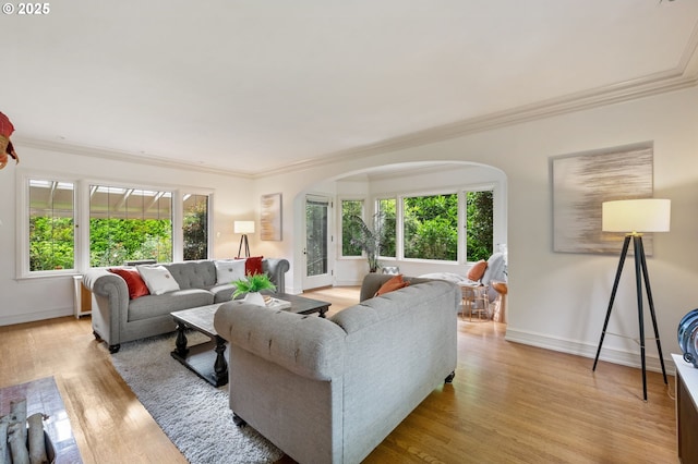living room featuring arched walkways, light wood-style flooring, crown molding, and baseboards