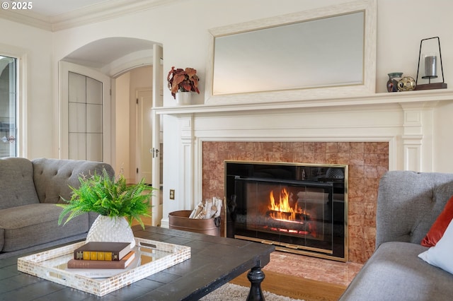living area with a fireplace, crown molding, arched walkways, and wood finished floors