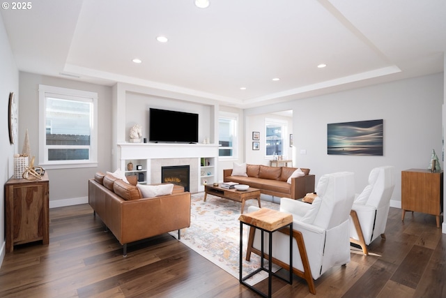 living room with dark hardwood / wood-style floors, a tile fireplace, and a raised ceiling