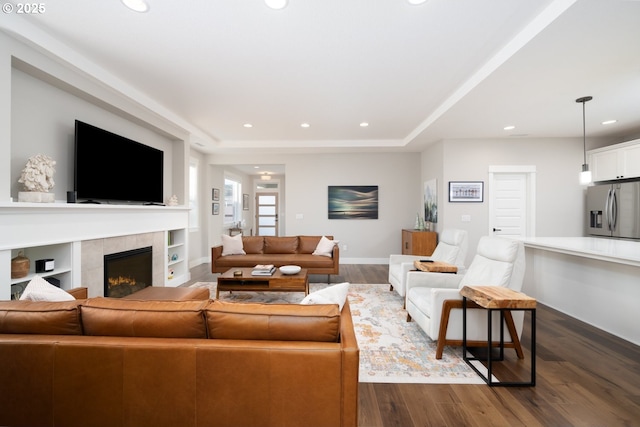 living room featuring dark wood-type flooring, a fireplace, and a tray ceiling