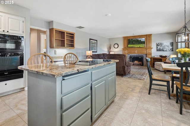 17958 Saint Clair Dr, Lake Oswego, OR 97034 - kitchen featuring black appliances, a fireplace, a center island with sink, light tile patterned flooring, and light stone counters