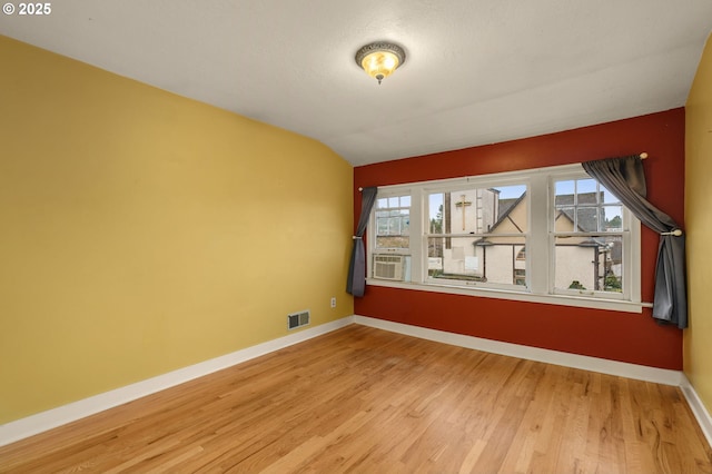 empty room featuring vaulted ceiling, visible vents, baseboards, and wood finished floors