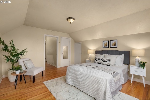 bedroom with vaulted ceiling, wood finished floors, and baseboards