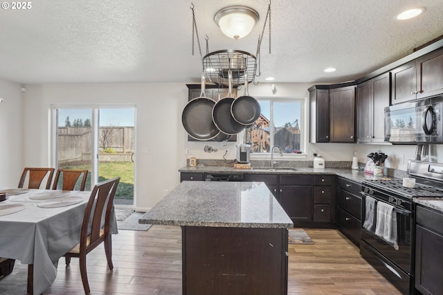 kitchen with sink, dark brown cabinets, a kitchen island, light stone countertops, and black appliances