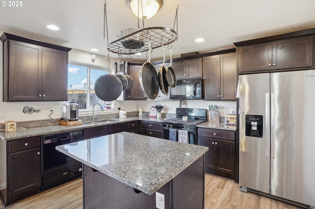 kitchen with sink, a kitchen island, light stone countertops, light hardwood / wood-style floors, and black appliances