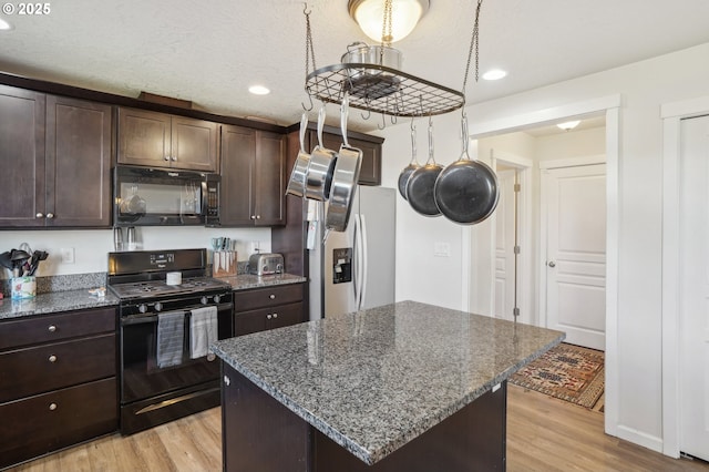 kitchen featuring dark brown cabinetry, black appliances, a center island, and dark stone counters