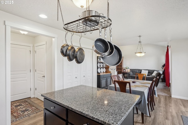 kitchen with light wood-type flooring, dark stone countertops, a center island, dark brown cabinets, and a textured ceiling