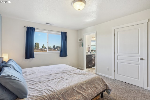 bedroom with ensuite bath, carpet floors, and a textured ceiling