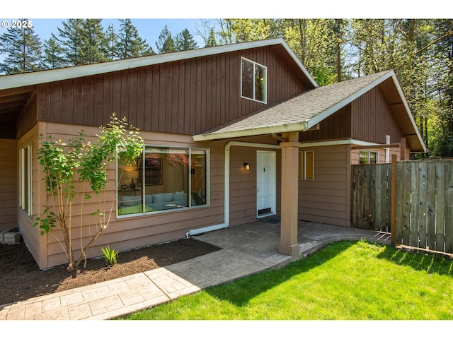 view of front facade with a shingled roof, a front lawn, a patio area, and fence