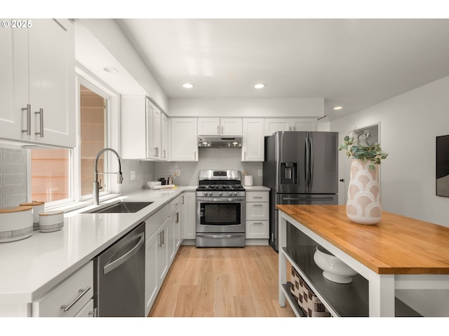 kitchen featuring appliances with stainless steel finishes, a sink, wood counters, under cabinet range hood, and white cabinetry