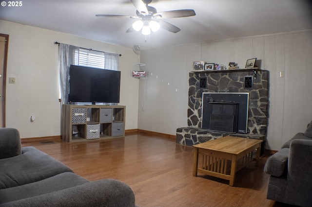 living room featuring wood-type flooring, a stone fireplace, wooden walls, and ceiling fan