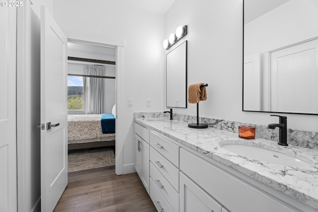 ensuite bathroom featuring a sink, double vanity, wood finished floors, and connected bathroom