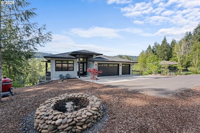 prairie-style home featuring board and batten siding, an attached garage, driveway, and an outdoor fire pit