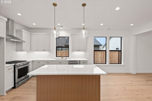 kitchen featuring white cabinetry, stainless steel appliances, wall chimney range hood, pendant lighting, and a center island