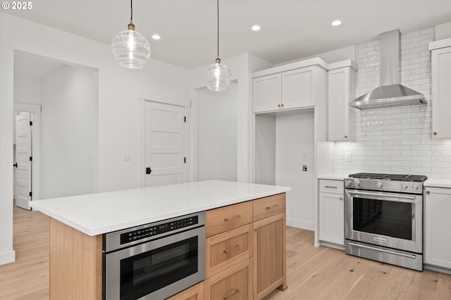 kitchen with white cabinetry, gas stove, backsplash, decorative light fixtures, and wall chimney exhaust hood