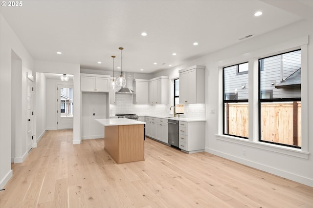 kitchen with pendant lighting, a kitchen island, light hardwood / wood-style flooring, stainless steel appliances, and wall chimney exhaust hood