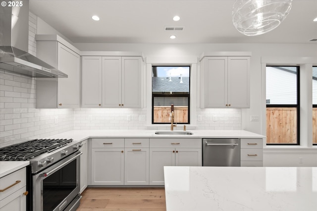 kitchen with appliances with stainless steel finishes, wall chimney exhaust hood, sink, and white cabinetry