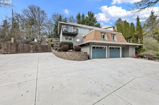 view of front of home with mansard roof, fence, concrete driveway, a shingled roof, and a balcony