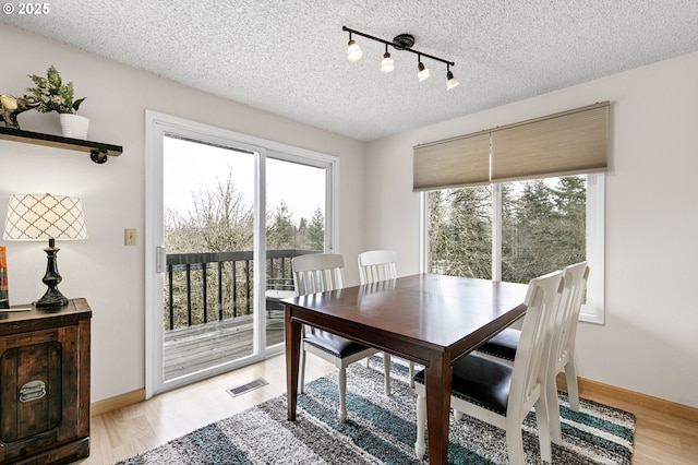 dining room with light wood-type flooring, visible vents, baseboards, and a textured ceiling