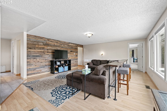 living room featuring visible vents, a textured ceiling, wood finished floors, wood walls, and an accent wall