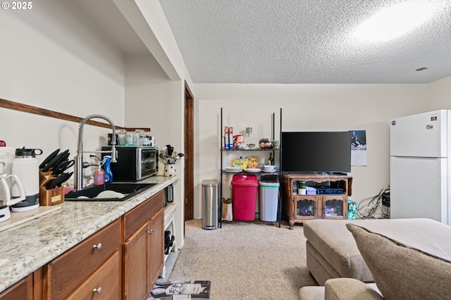 kitchen featuring brown cabinetry, freestanding refrigerator, a textured ceiling, light colored carpet, and open floor plan