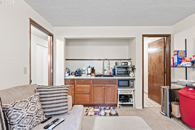 kitchen featuring brown cabinetry, light carpet, a textured ceiling, and a sink