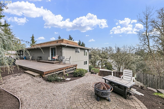 rear view of property featuring a patio, fence, a wooden deck, mansard roof, and a fire pit