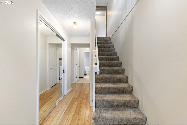 stairway featuring baseboards, a textured ceiling, and wood finished floors