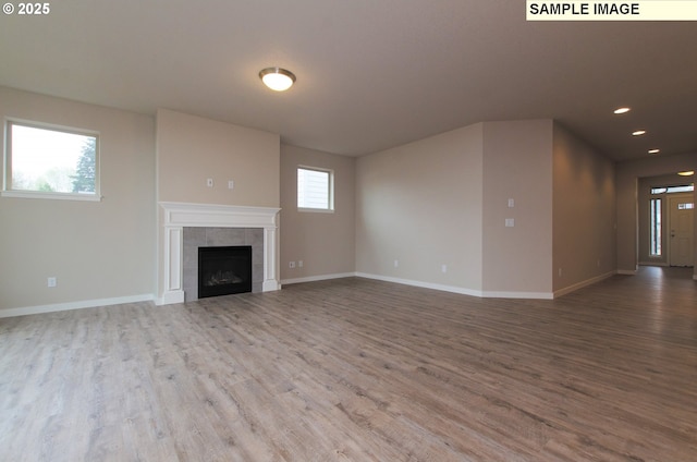 unfurnished living room with wood-type flooring and a tiled fireplace