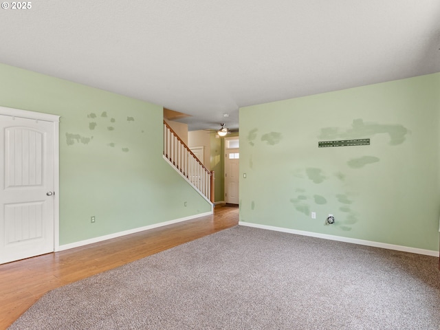 carpeted spare room featuring wood finished floors, baseboards, ceiling fan, and stairs