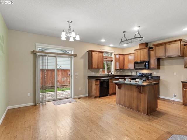 kitchen featuring brown cabinetry, light wood finished floors, an inviting chandelier, black appliances, and dark countertops