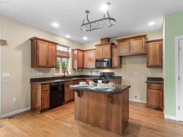 kitchen featuring dark countertops, visible vents, brown cabinetry, black appliances, and a sink