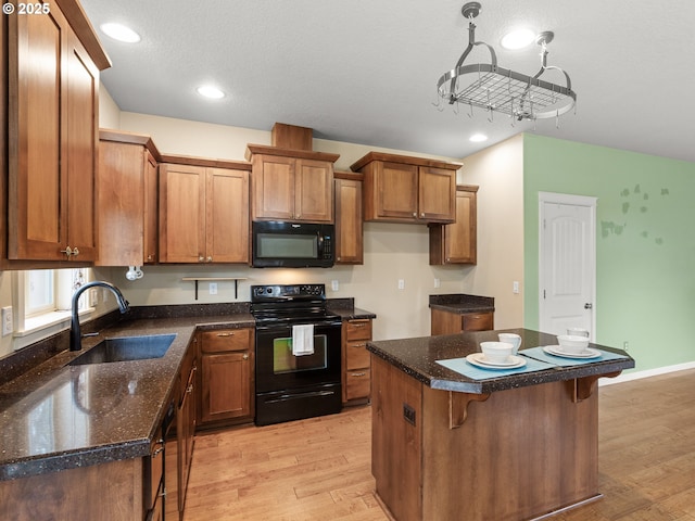 kitchen with brown cabinetry, a kitchen island, a sink, black appliances, and light wood-style floors