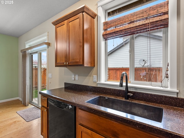 kitchen with black dishwasher, dark stone countertops, brown cabinets, light wood-style floors, and a sink