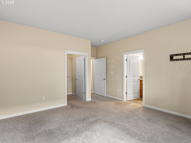 unfurnished bedroom featuring a spacious closet, connected bathroom, baseboards, and light carpet