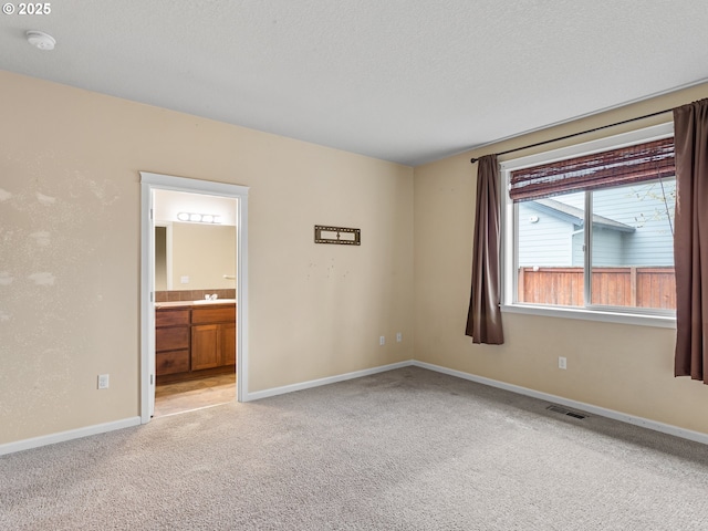 unfurnished room with baseboards, visible vents, a sink, a textured ceiling, and light carpet