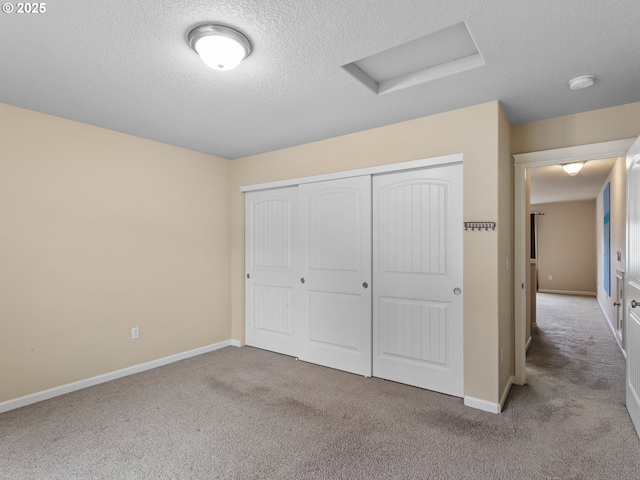 unfurnished bedroom with baseboards, carpet floors, attic access, a closet, and a textured ceiling