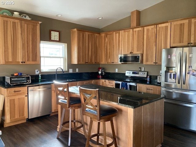 kitchen with dark hardwood / wood-style flooring, stainless steel appliances, vaulted ceiling, sink, and a kitchen island