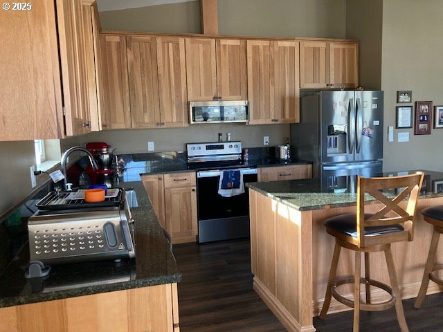 kitchen featuring dark hardwood / wood-style floors, dark stone countertops, light brown cabinetry, appliances with stainless steel finishes, and a kitchen island