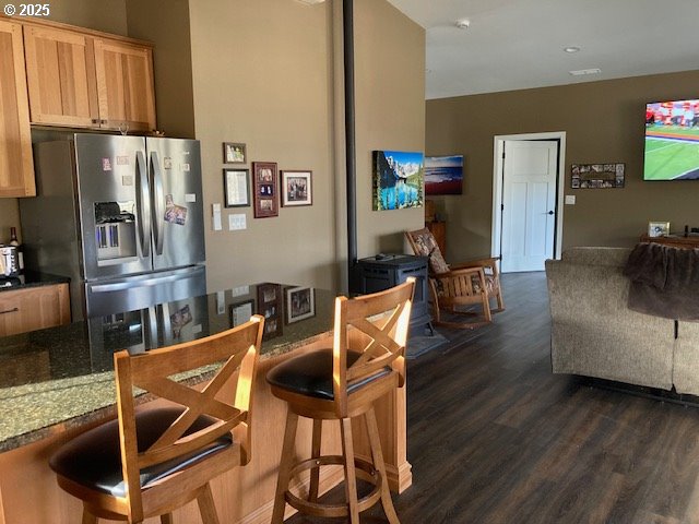 kitchen featuring dark stone countertops, light brown cabinets, dark wood-type flooring, and stainless steel refrigerator with ice dispenser