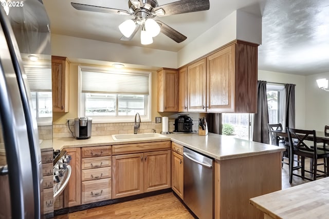 kitchen with appliances with stainless steel finishes, a sink, light countertops, a peninsula, and a ceiling fan