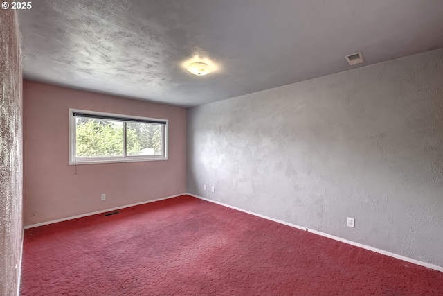 spare room featuring baseboards, dark colored carpet, and visible vents