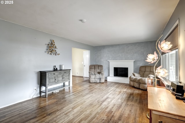 living area featuring baseboards, a fireplace with raised hearth, and wood finished floors