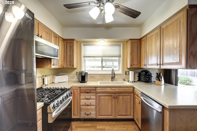 kitchen with a ceiling fan, a sink, light countertops, stainless steel appliances, and light wood-style flooring